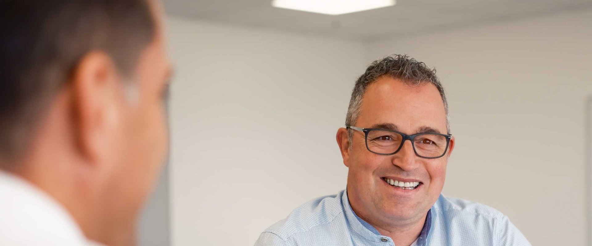 Lächelnder Mann mit Brille und hellblauem Hemd im Büro