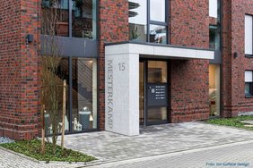 Eingangsbereich in Beton-Optik und purenit-Kern, größeres Gebäude mit Klinkerfassade und Fenstern